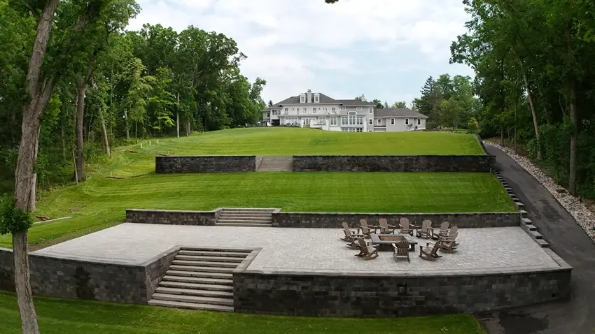 "Impressive retaining wall and patio built into a steep hillside in Lake Country, Wisconsin. This grand design seamlessly integrates with the landscape, offering stunning views and a perfect space for outdoor gatherings. #LakeCountry #RetainingWall #PatioDesign #HillsideLiving"