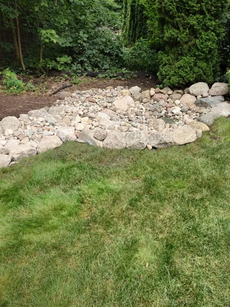 This image features a drainage solution with a stone bed installed in Chenequa, WI. The system includes a network of stones designed to efficiently manage and channel water runoff, preventing erosion and water accumulation. The stone bed not only enhances the functionality of the drainage system but also adds a natural, aesthetically pleasing element to the landscape, ensuring effective water management while blending seamlessly with the surroundings.