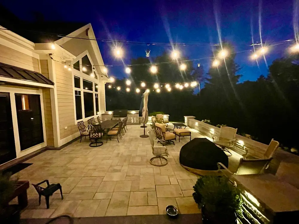 "Experience the magic of outdoor living with a stunning night-time patio setup. Adorned with string lights, downlighting, elegant pillars, and cozy seat walls, this space creates a perfect ambiance for evening gatherings. #OutdoorLiving #PatioDesign #StringLights #Downlighting #EveningAmbiance"