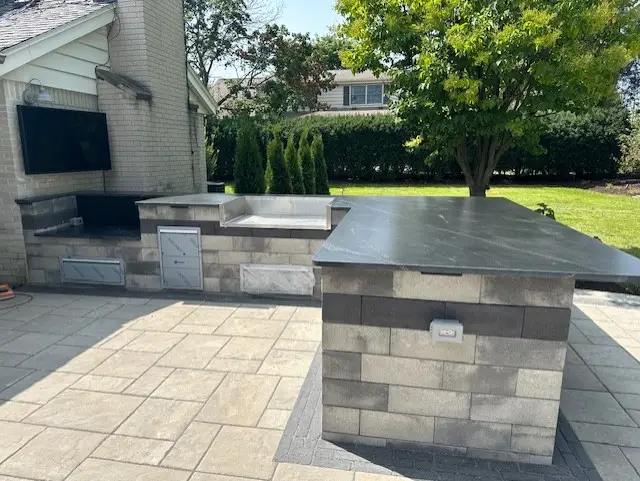 "Stunning outdoor kitchen in Elm Grove, WI, featuring an L-shaped breakfast bar with a dedicated grille area and a beautifully crafted paver patio. This design creates a perfect space for dining and entertaining outdoors. #ElmGroveWI #OutdoorKitchen #BreakfastBar #PaverPatio #GrilleArea"