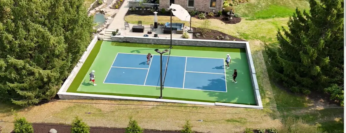 Professional pickleball court installation in Milwaukee WI by Liban Landscape featuring premium surface, lighting, and retaining walls. Pickleball Court Installation in Milwaukee, WI: The Liban Landscape Difference Pickleball is more than just a game—it’s a community, a passion, and for many, a lifestyle. As its popularity continues to surge in Milwaukee, WI, the demand for professional pickleball courts has never been higher. Liban Landscape, known for transforming outdoor spaces with beautiful and functional designs, is stepping into the spotlight with their expert pickleball court installations. In partnership with Premier Turf & Greens, our team delivers a comprehensive, high-quality approach to building pickleball courts that bring the fun and excitement of the game right to your backyard or neighborhood. Whether you're looking for a private pickleball court to enjoy with family and friends or planning a community space that caters to avid players, Liban Landscape has the expertise, tools, and dedication to create the ideal court for your needs. Our pickleball courts are designed with precision, creativity, and durability in mind, ensuring that every detail—from the surface to the lighting—is perfect. Why Choose Liban Landscape for Your Pickleball Court? Building a professional pickleball court involves more than just a flat surface and a net. At Liban Landscape, we take pride in offering a comprehensive approach to pickleball court installation, combining expert design, precise construction, and premium materials to create a court that not only looks stunning but also performs exceptionally well. Here’s why we’re the best choice for your pickleball court installation in Milwaukee, WI. Custom Design and Layout Every pickleball court we build starts with a detailed design process. We work closely with our clients to understand their vision and needs, ensuring the court fits seamlessly into the existing landscape. Whether you're looking for a single-court setup for your backyard or a multi-court complex for a commercial property, we’ll design a layout that maximizes the available space while creating a visually appealing and functional playing area. Our design process includes everything from surface materials and striping to custom lighting solutions and surrounding landscaping elements. We aim to create an environment that enhances the game and provides an inviting space for both players and spectators. Premium Sports Surface Coating One of the most important aspects of a pickleball court is the playing surface. Liban Landscape uses Premium Sports Surface Coating to ensure that your court delivers the best performance and durability. This high-quality surface provides excellent grip, ball response, and shock absorption, making it perfect for intense matches and daily play. Plus, it comes in a variety of color options, allowing you to customize the look of your court to match your style or branding. Professional Installation and Grading A well-built court starts with proper grading and preparation. Our expert team at Liban Landscape ensures that the ground is perfectly leveled and properly graded to promote drainage and prevent water accumulation—both of which are crucial for maintaining the integrity and longevity of your court. We pay close attention to every aspect of the installation process, from the sub-base to the final surface application, guaranteeing a smooth, flawless playing area. Full Sports Lighting for Day and Night Play Pickleball is a game that should be enjoyed at any time of the day, which is why we offer full sports lighting solutions as part of our installation package. Our advanced lighting systems provide consistent, even illumination across the entire court, ensuring that players can continue their games long after the sun has set. The lighting we install is energy-efficient and designed to withstand the elements, so you can enjoy night games without worrying about frequent maintenance or high energy costs. Retaining Walls and Spectator Areas One of the unique features we offer is the integration of custom retaining walls and seating areas into your pickleball court design. A retaining wall can serve both functional and aesthetic purposes, providing necessary support for sloped terrain while adding a sleek, modern touch to your outdoor space. Additionally, we can create dedicated spectator areas—like the hecklers' patio seen in our Elm Grove, WI project—so friends and family can comfortably watch the action from a prime vantage point. Durable and Weather-Resistant Materials Milwaukee’s weather can be unpredictable, with cold winters and hot summers taking their toll on outdoor surfaces. That’s why we use only the highest quality, weather-resistant materials for our pickleball courts. From the surface coatings to the net systems, every element is chosen for its ability to withstand the elements and maintain its performance and appearance over time. Featured Project: Pickleball Court Installation in Elm Grove, WI Recently, Liban Landscape, in collaboration with Premier Turf & Greens, completed an extraordinary pickleball court project in Elm Grove, WI. This court is a shining example of our dedication to quality, design, and craftsmanship. From the moment you see the aerial footage of this court, it’s clear that no detail was overlooked. The sleek, vibrant striping on the premium sports surface and the strategic placement of full sports lighting allow for flawless gameplay, day or night. But the real standout feature? The custom retaining wall with stylish down lights that elevate the court’s visual appeal while providing practical functionality. And for those who enjoy watching the game as much as playing it, the hecklers' patio offers a comfortable, elevated viewing area, perfect for cheering on players or simply soaking in the pickleball action. This project highlights the Liban Landscape difference—combining form and function to create outdoor spaces that aren’t just beautiful, but designed for real-world enjoyment and long-term durability. Planning Your Pickleball Court for Spring and Summer 2025 The demand for high-quality pickleball courts is on the rise, and now is the time to plan your project for Spring and Summer 2025. Whether you're looking to enhance your backyard with a private court or create a community space where neighbors can come together for friendly matches, Liban Landscape is ready to make your vision a reality. We offer flexible scheduling and personalized design consultations to ensure that your court is completed on time and to your exact specifications. As part of our commitment to customer satisfaction, we take the time to listen to your ideas and provide expert guidance throughout the process, from design to installation. Don't wait until it’s too late—secure your spot now to ensure your pickleball court is ready for next year’s prime playing season. How Liban Landscape Stands Out in Pickleball Court Installation Liban Landscape brings a unique combination of landscaping expertise and sports surface knowledge to every pickleball court project we undertake. We believe that creating the perfect court is about more than just installing a surface—it’s about crafting an environment that enhances the game and the overall experience for players and spectators alike. Here’s how we stand out: Comprehensive Design Services: We take a holistic approach to court design, ensuring that the entire space works together seamlessly, from the surface and lighting to surrounding landscaping and seating areas. High-Quality Materials: We use only premium materials for every aspect of the court, ensuring durability, weather resistance, and optimal performance. Expert Installation: Our experienced team handles all aspects of the installation, including grading, surface application, lighting installation, and finishing touches, to ensure a flawless final product. Customization Options: No two pickleball courts are the same. We offer a range of customization options, from court colors and striping to spectator seating and retaining walls, allowing you to create a truly unique space. FAQs What surfaces do you use for pickleball courts? We use Premium Sports Surface Coating, known for its excellent grip, durability, and resistance to weather. It’s designed to provide the best playing conditions while withstanding the elements. Can I customize the design of my pickleball court? Absolutely! We offer fully customized design options, including court layout, surface colors, lighting, and even additional features like retaining walls and spectator areas. How long does it take to install a pickleball court? The timeline varies depending on the size and scope of the project, but most courts are completed within 4 to 8 weeks from the start of construction. Do you offer court lighting for nighttime play? Yes, we install full sports lighting systems that provide excellent visibility for evening games. Our lighting solutions are energy-efficient and designed for long-lasting performance. What areas do you serve? We primarily serve Milwaukee, WI, and surrounding areas, including Elm Grove. However, we’re open to discussing projects throughout Wisconsin. What maintenance is required for a pickleball court? Our courts are designed to be low-maintenance, but we recommend periodic cleaning and inspections to ensure the surface remains in good condition and free from debris. Conclusion Liban Landscape is proud to offer top-tier pickleball court installation services in Milwaukee, WI, combining our expertise in landscape design with advanced sports surface technology to create courts that are beautiful, durable, and fun to play on. Whether you're a seasoned player or new to the game, our custom pickleball courts provide the perfect space for enjoying this fast-growing sport. Ready to create your own pickleball paradise? Contact Liban Landscape today to start planning your court for Spring and Summer 2025, and let us transform your outdoor space into a pickleball destination that’s built to last. Suggested Internal Links: Custom Retaining Walls Patio and Walkway Installation Suggested Outbound Links: Pickleball Court Maintenance Tips [Official Pickleball Rules](https AIPRM Premium - ChatGPT Prompts   Favorites   AIPRM Public Own   Hidden   Add List Topic Activity Sort by Model Create A Content Calendar Copywriting / Accounting · The Plug · 7 months ago 100% Yoast SEO Optimized Blog Writer Helpful Content Marketer ready to Create A Content Calendar For Social Media Platforms   1.1K   456   0   Add Public Prompt