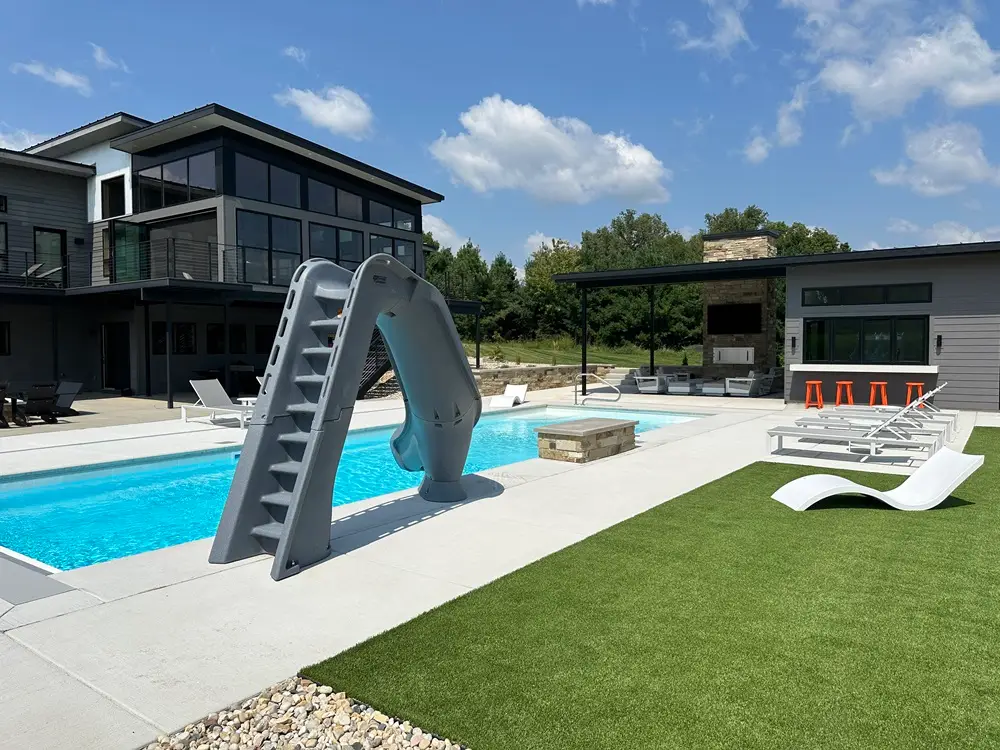 "Stunning pool landscape featuring a charming outhouse, cozy fireplace, elegant seat walls, lush artificial turf, and a stylish fire pit. This versatile design creates a perfect blend of functionality and relaxation, enhancing your outdoor living experience. #PoolLandscape #OutdoorLiving #Fireplace #SeatWalls #ArtificialTurf #FirePit"